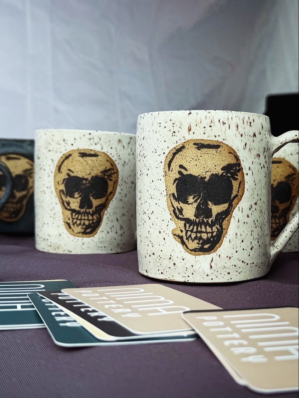 Skull-themed mugs on a table with NIMA business cards